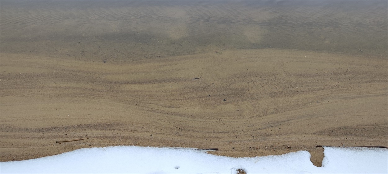 Буг малює візерунки піском у прозорій воді. Зимовий пляж Южноукраїнська