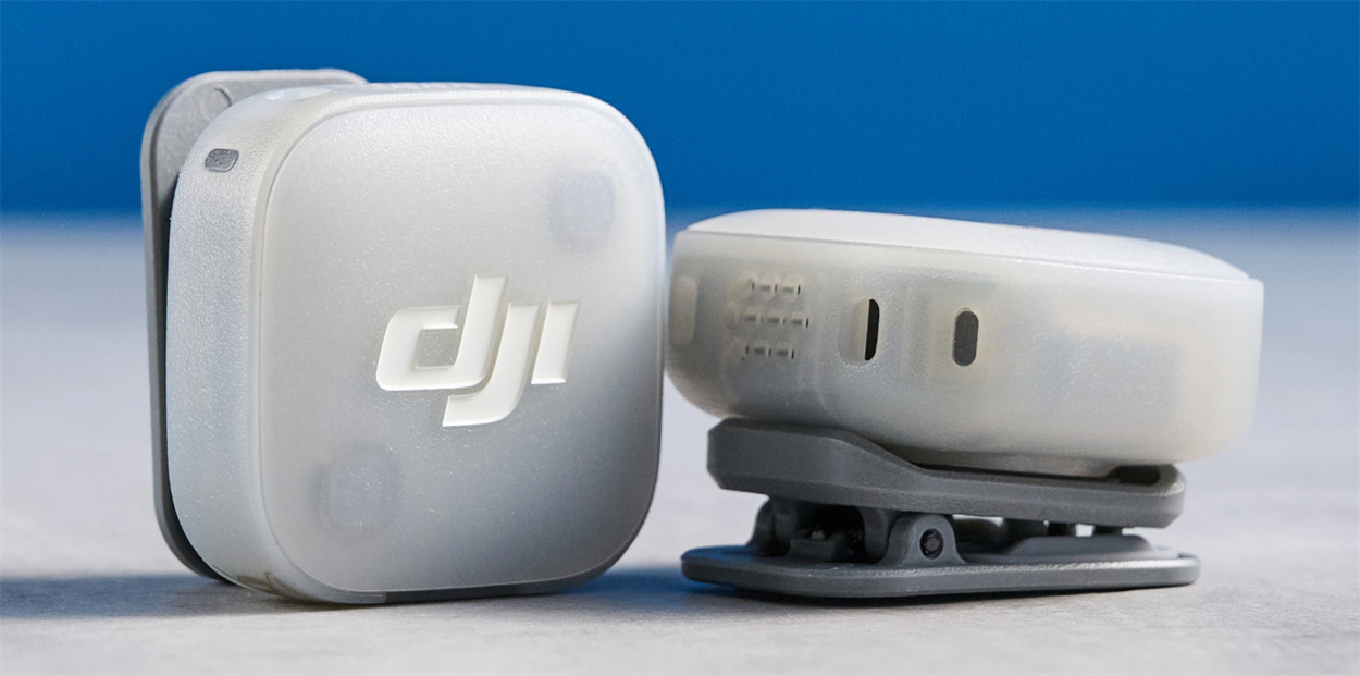 Два білі трансмітери DJI Mic Mini 2 крупним планом: один повернутий лицьовою кришкою з логотипом, другий — зворотним боком, де видно поворотну сіру кліпсу та два магнітні контакти.